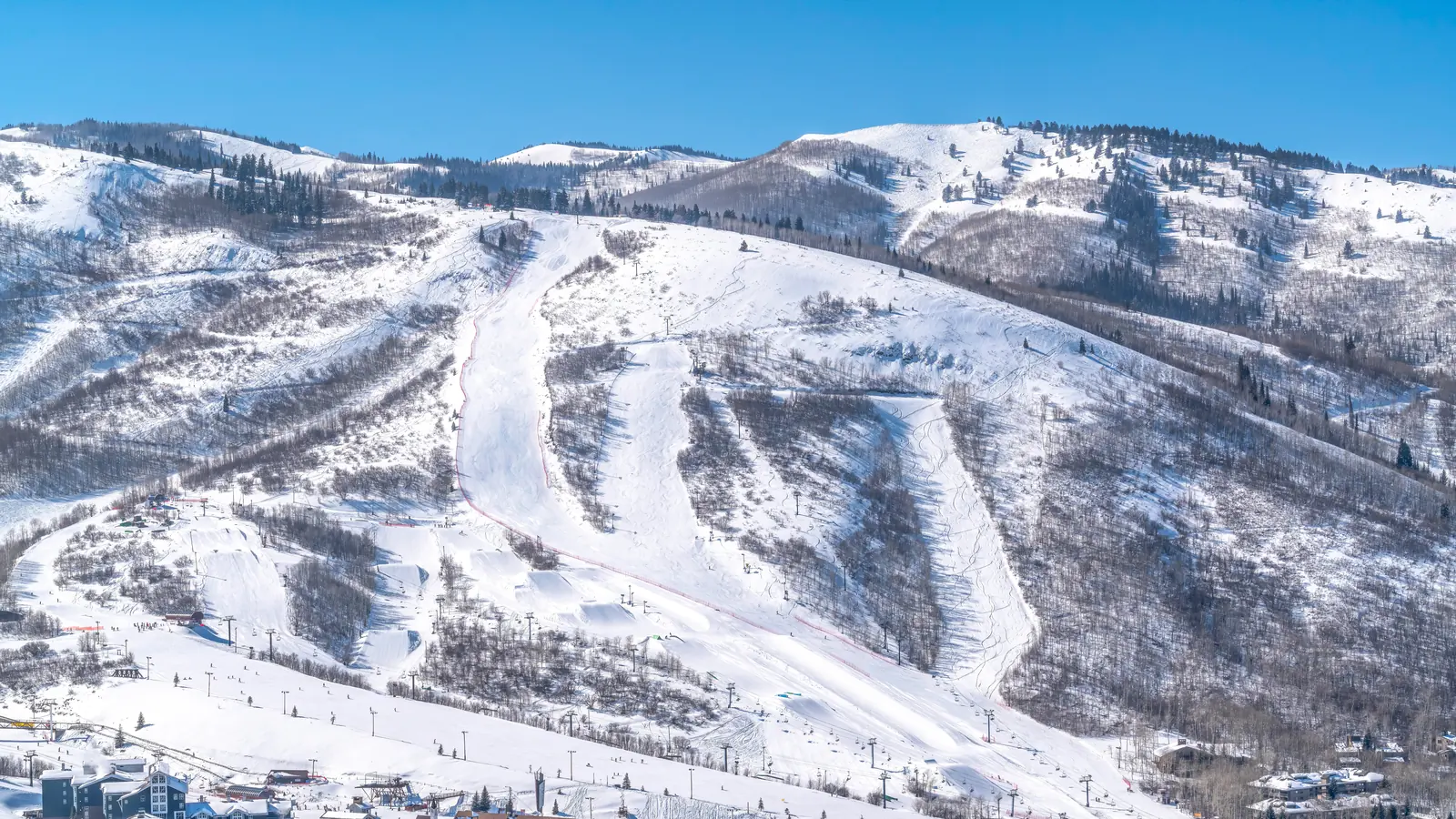 Groomed ski runs curving down a snow-covered mountain above a resort base village under a clear blue sky