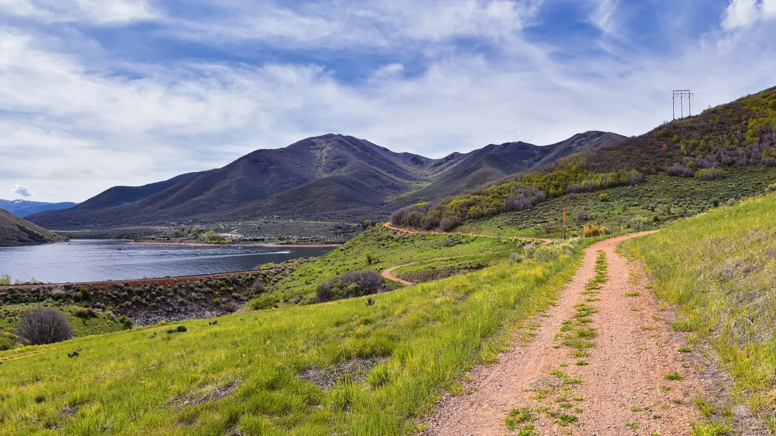 A dirt trail following the shore of Deer Creek Reservoir, with green foothills and mountains beyond