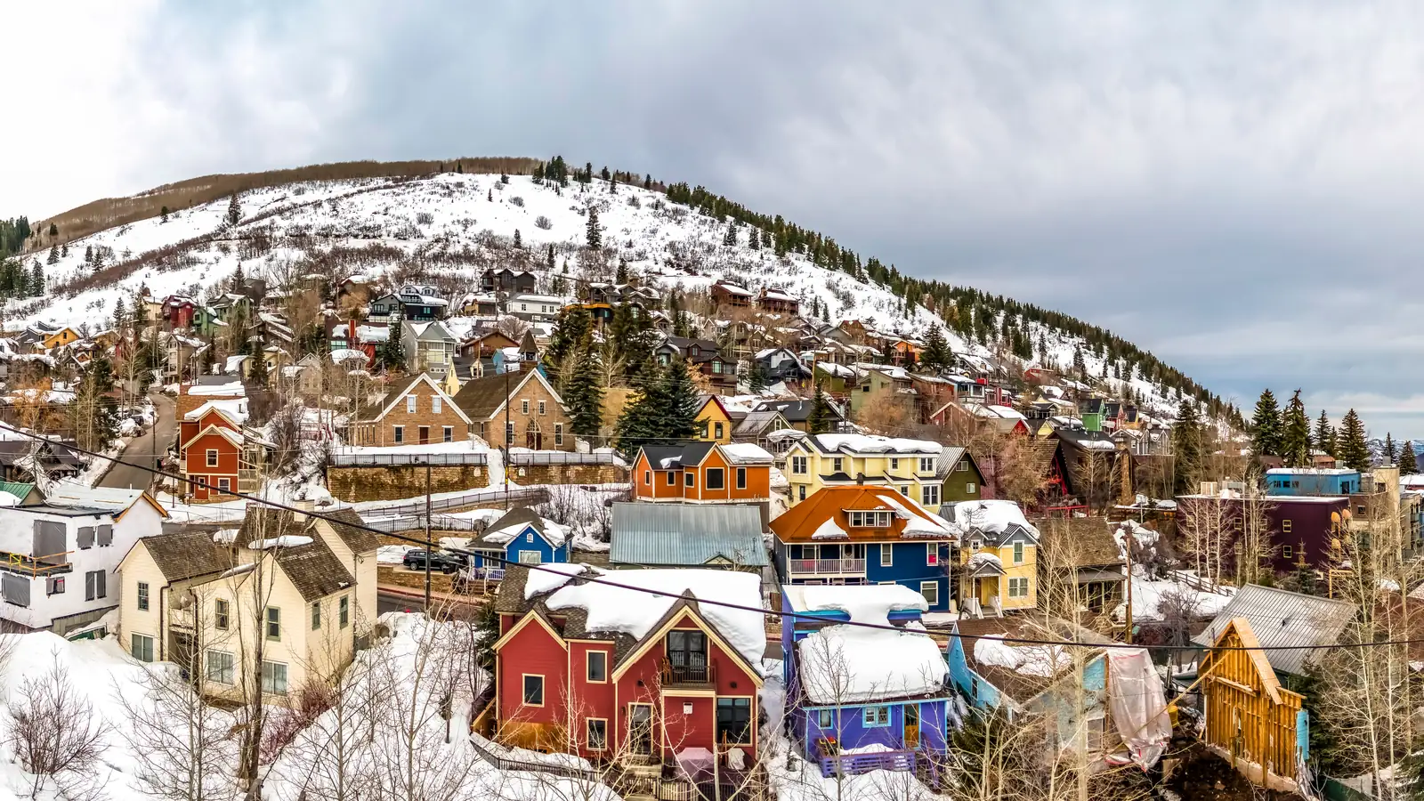 Colourful historic houses on a snowy hillside in Old Town Park City, with pines and a ridgeline rising behind them