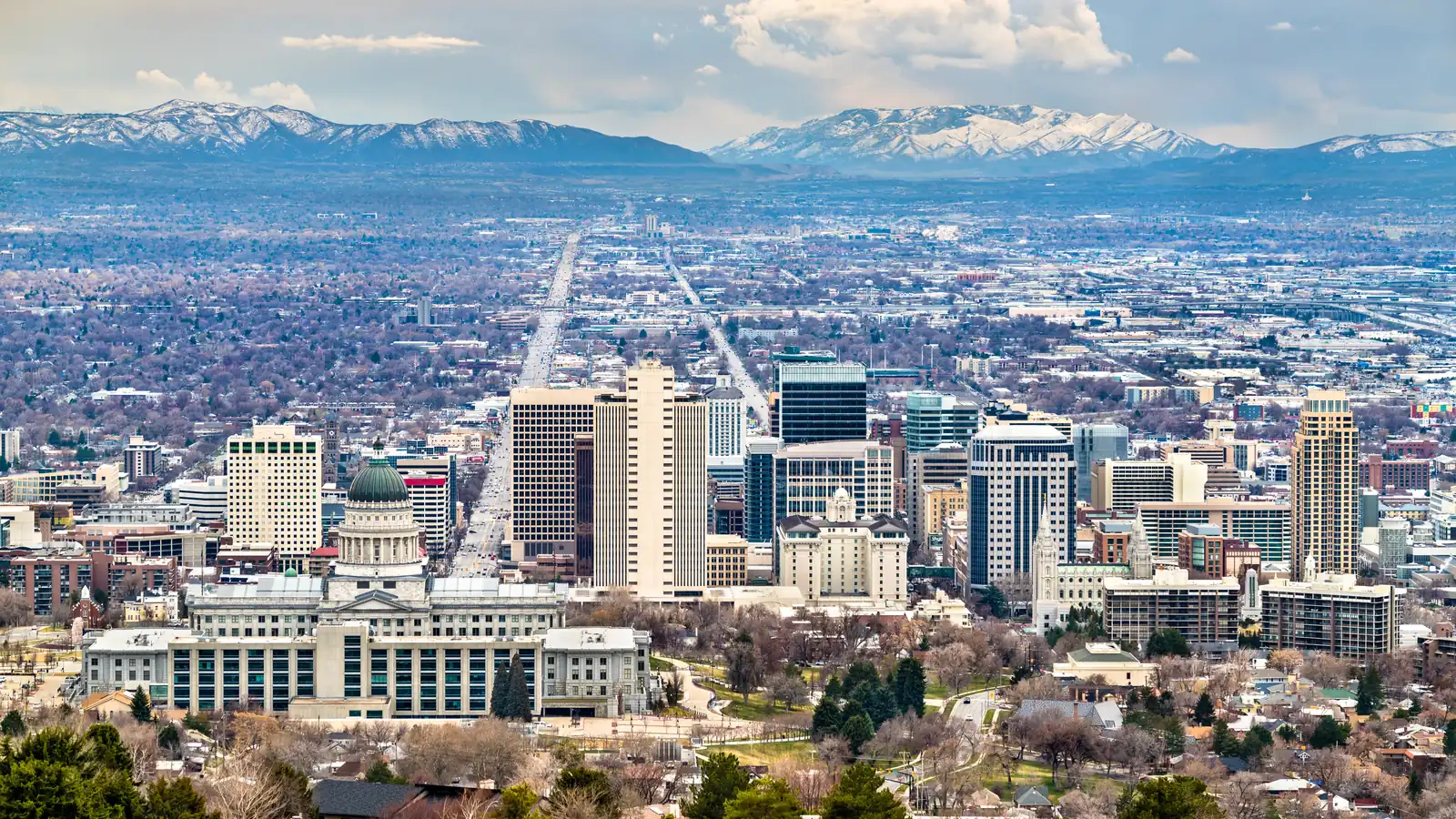 Downtown Salt Lake City seen from above, with the snow-capped Wasatch Range stretching behind the skyline