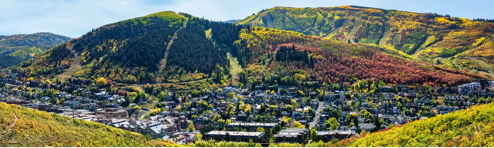 Park City in autumn, the town spread below hillsides of yellow and red aspens with ski runs cut into the mountains behind